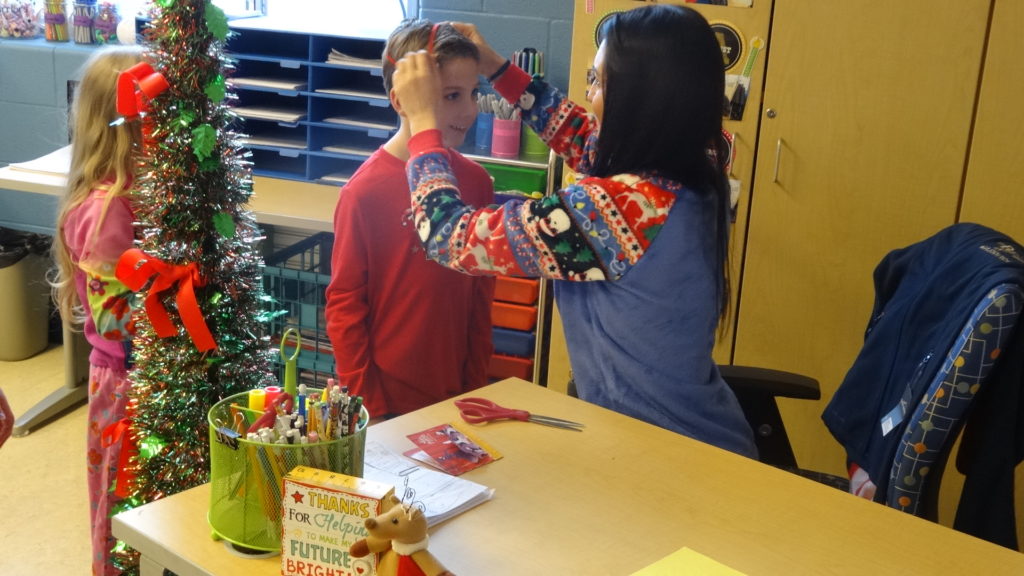 Second-grade teacher Natalie Huda helps Greyson Berena put on his "The Polar Express" bell. Lilliana Case awaits her turn.