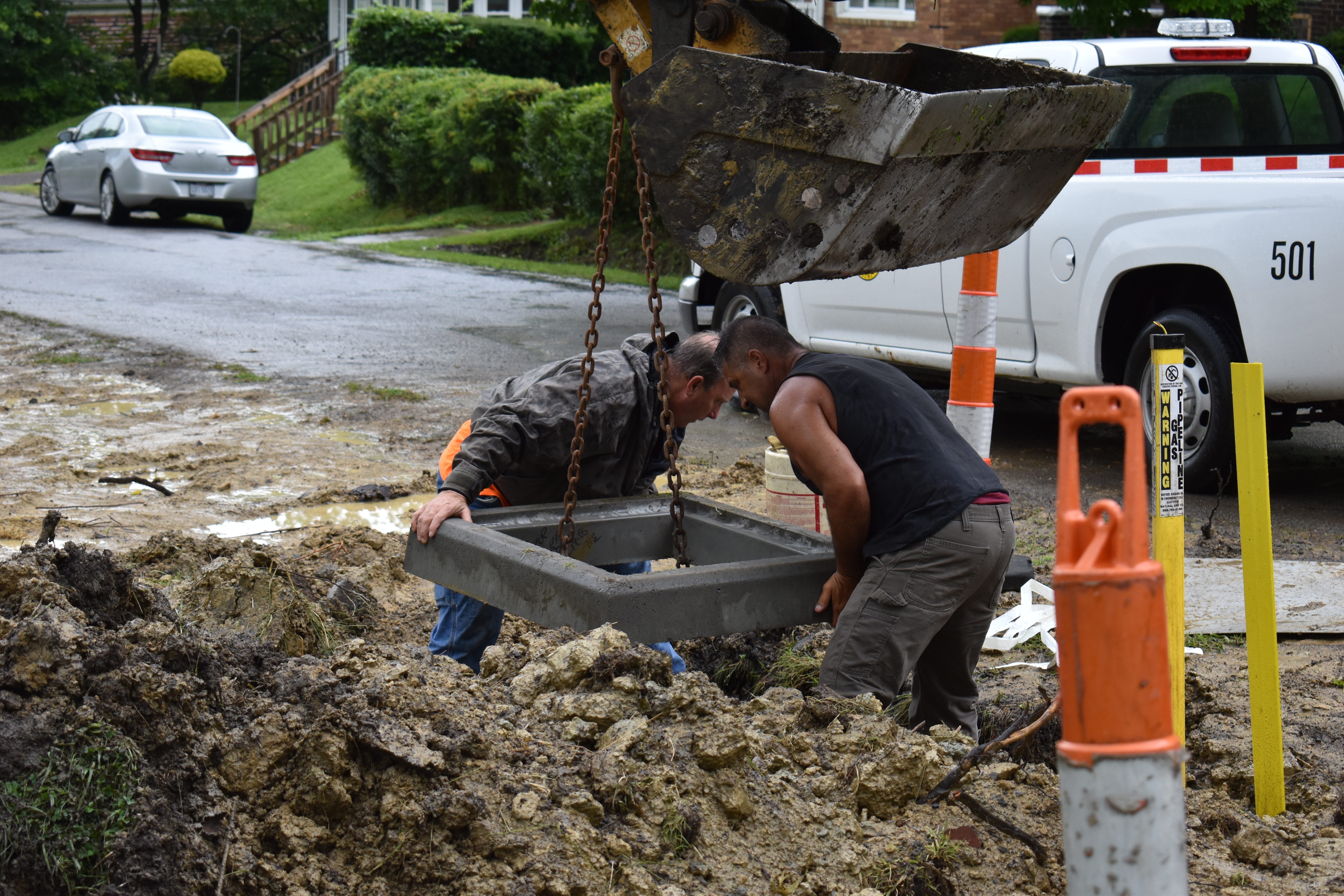 Brookfield Road Superintendent Jaime Fredenburg, left, and D.J. Mild position the top of a catch basin being lowered by backhoe operator Matt O'Dell during a drainage project at Hazelton and Davis Streets.