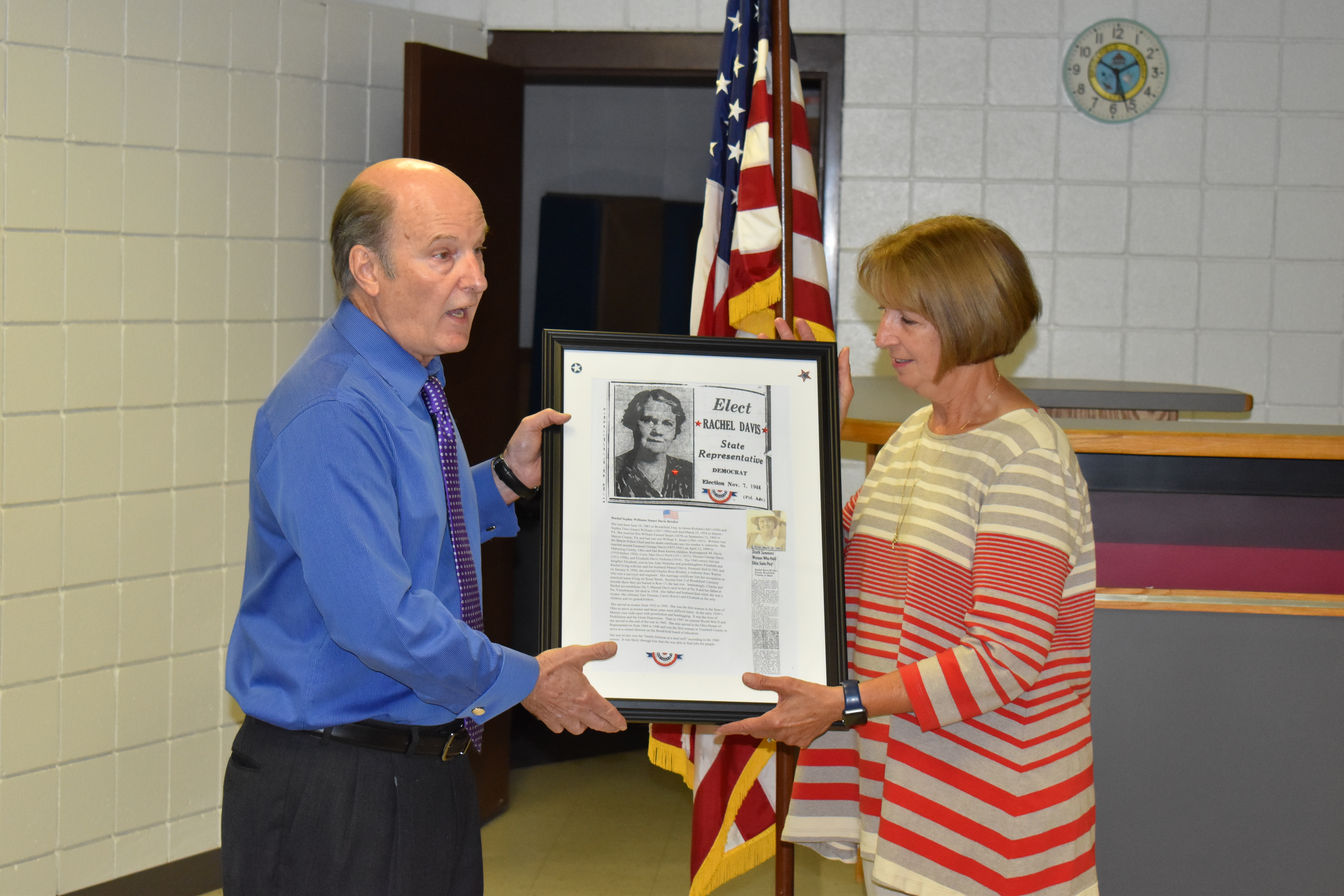 Brookfield Trustee Gary Lees presents a photo and information about former Trustee Rachel Bricker to Barbara Stevens, president of the Brookfield Historical Society.