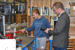 Brookfield High School sophomore Josh Schell shows Mike Kahoe, a representative of the lieutenant governor's office, where to place the block he has picked up with a robotic arm.