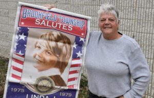 Linda Fedorko holds the veteran's banner that her wife, Shawna, had placed on the green in Brookfield Center. The banners are a fundraiser for the Brookfield Township Historic Commission.