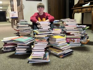 Trent Litman sits among piles of books collected to be given to patients at Akron Children's Hospital. Contributed photo.