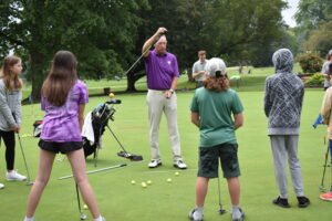 Bob Collins holds his putter like a pendulum to show middle school students how they should swing their arms when putting.
