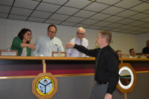 Brookfield Police Sgt. Aaron Kasiewicz, reaches to shake the hand of Trustee Shannon Devitz. Also shown are Trustees Mark Ferrara, second from left, and Dan Suttles.