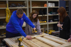 Hunter Hoskin uses an impact driver to attach pieces of bed frame in his Brookfield High School home improvement class. Also shown are Alyvia Carpec, right, and Makayla Plato.